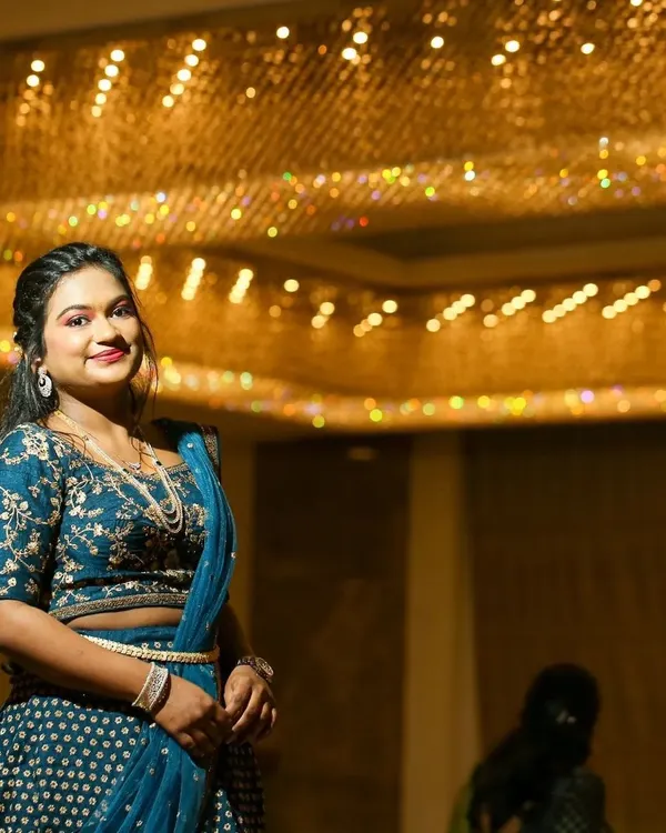 A stunning reception look under dramatic lighting. The bride wears an embroidered blue lehenga, and her makeup features a defined eye and a warm lip color, creating a chic and polished style.