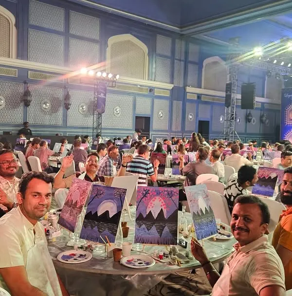 A table of happy employees from a corporate conference, proudly showing off their mountain landscape paintings. It's amazing to see how a little paint can spark so much conversation and teamwork.