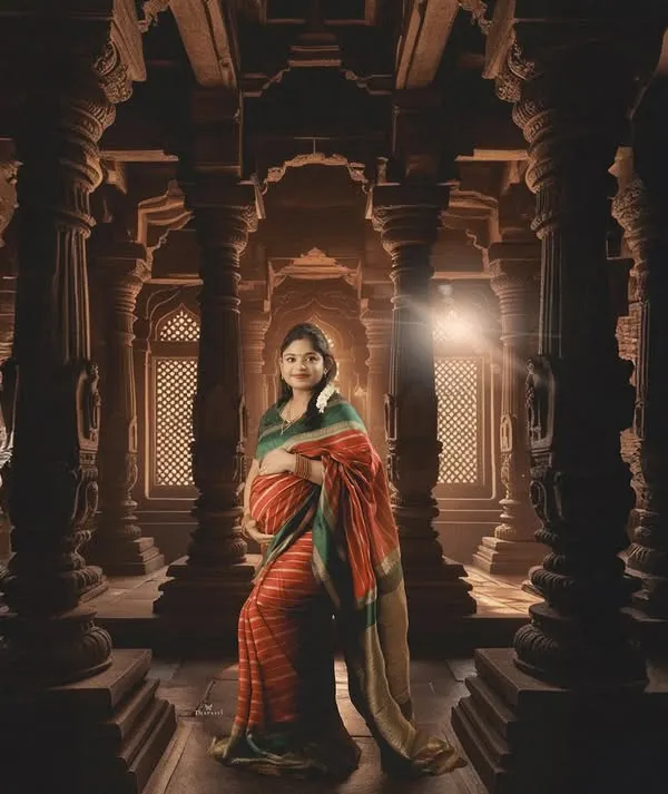 A powerful portrait set within a grand, traditional temple-style hall. The intricate pillars and dramatic lighting create a sense of heritage and divine grace for this maternity photo.