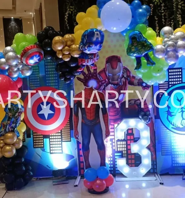 An action-packed Avengers photo booth with a city skyline backdrop, character cutouts of Iron Man, Captain America, and Hulk, and a light-up number '3'.