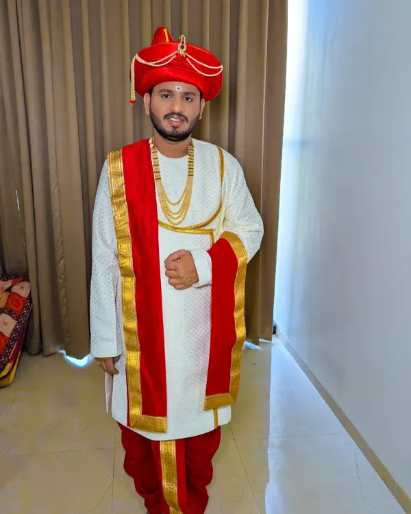 A classic Maharashtrian groom in a Peshwai look. The red turban, simple white kurta, and traditional jewelry create a timeless and regal appearance for the wedding vidhi.