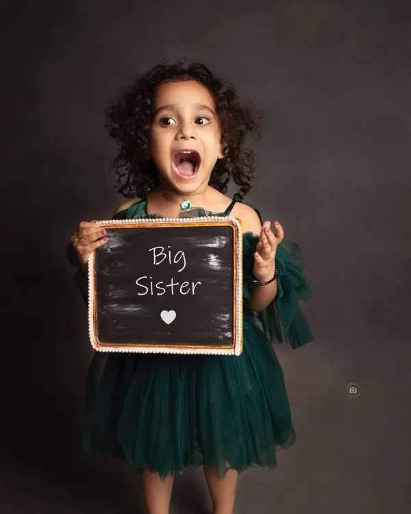 The pure excitement of becoming a big sister! Her expressive face says it all in this fun and memorable announcement photo.