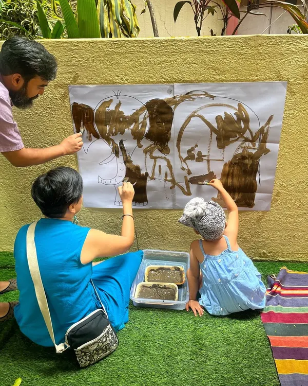 I believe play is a powerful way for families to connect. Here, parents and a child work together on a large-scale mud painting, turning a simple art activity into a memorable bonding experience.
