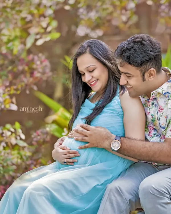 An expecting couple shares an intimate moment in a lush garden setting. This outdoor maternity portrait uses natural light to create a soft and romantic feel.