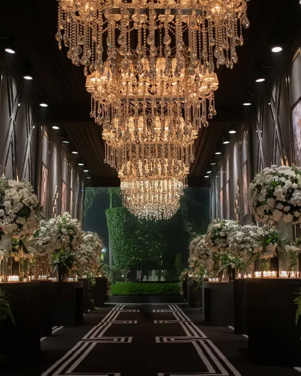 A dramatic entrance for a cocktail night, lined with massive arrangements of white flowers and candles. The path is crowned with a row of magnificent crystal chandeliers, creating a tunnel of light.