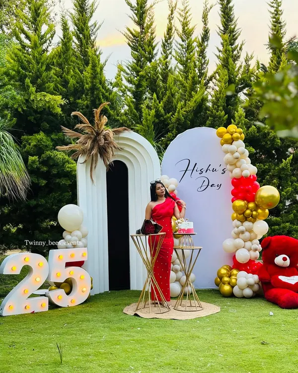A stunning outdoor setup for Hishu's 25th birthday. We used modern arched backdrops, a vibrant red, white, and gold balloon arrangement, and large marquee numbers to create a chic and celebratory photo zone.