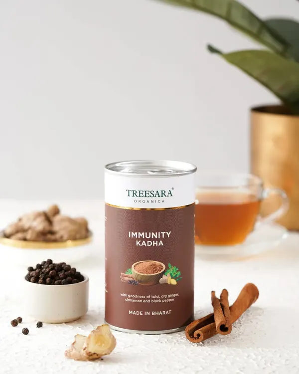 A beautifully styled shot of Immunity Kadha powder, surrounded by its core ingredients: cinnamon, black pepper, and ginger. This composition visually communicates the product's natural and healthful properties.