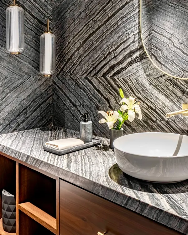 A closer look at the dramatic book-matched granite in the Parishram residence powder room. The dynamic veining of the stone is complemented by minimalist pendant lights and a simple vessel sink.