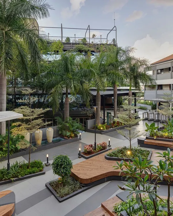 An aerial view of the completed landscape at Atria University. The design features organically shaped wooden decks that double as seating, surrounded by lush planters and mature palm trees, creating a vibrant campus hub.