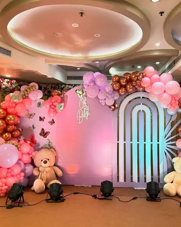 A gorgeous butterfly-themed baby shower, featuring a large backdrop with butterfly wing cutouts and a "Oh Baby" sign. The decor is a beautiful mix of pink and rose gold balloons, with two teddy bears adding a touch of cuddly sweetness.