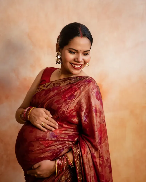 The radiant glow of an expecting mother is undeniable. This close-up shot in a beautiful red saree captures the pure happiness and excitement of this special time.
