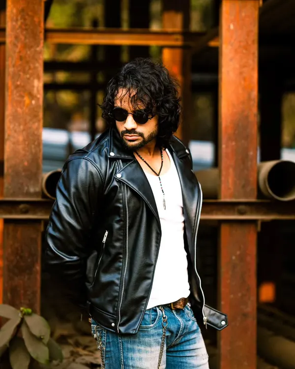 A rugged, outdoor portrait with a classic biker jacket. The industrial background and warm sunlight create a masculine and cinematic vibe.