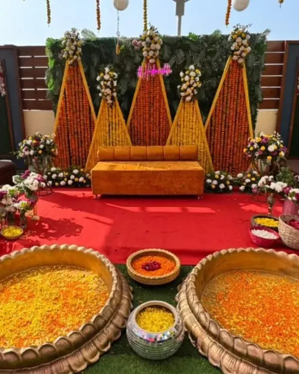 A classic Haldi setup with a modern twist. We used strings of orange and yellow marigolds to create a vibrant backdrop, paired with a comfortable mustard yellow sofa and large brass urlis filled with flower petals.