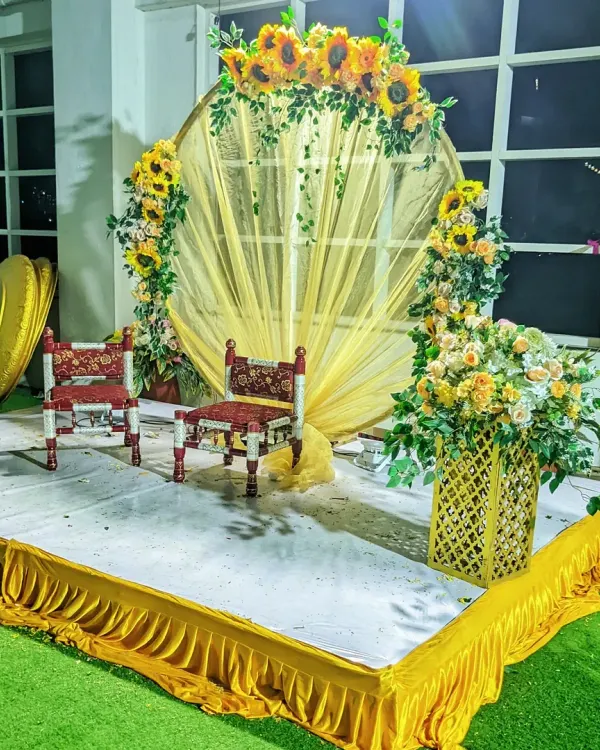 A classic Haldi ceremony stage. This setup features a circular backdrop with yellow drapes and is decorated with bright sunflower arrangements to match the traditional yellow theme.