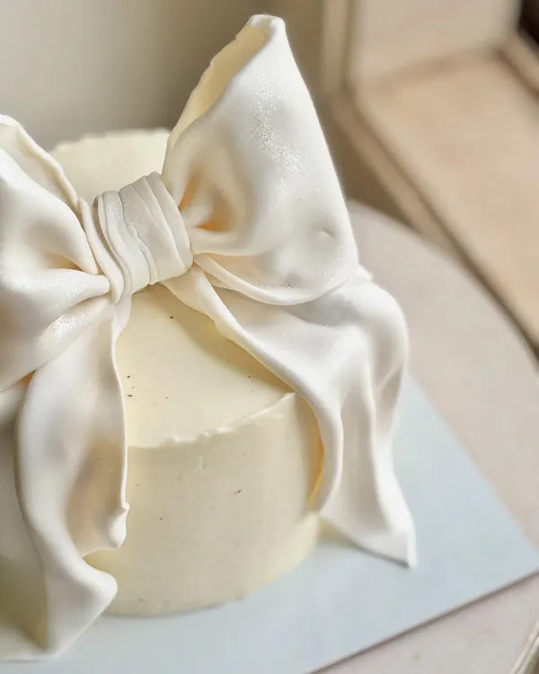 A close-up of the hand-sculpted fondant bow, showing the realistic fabric-like folds and texture. This detail is what gives the cake its couture feel.