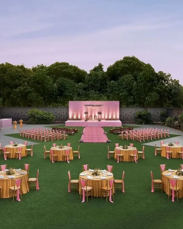 Another perspective of a grand lawn setup, showing the harmonious arrangement of guest seating and the main stage. The pastel pink and gold color scheme creates a light and elegant ambiance, perfect for a daytime corporate function or evening gala.