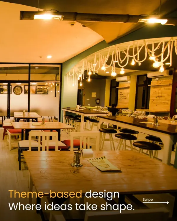 This wide shot of the Sattviko Idea Café showcases the theme-based design. The space is organized into different zones, including a long community table and smaller group tables, with unique overhead lighting to foster an environment where ideas can take shape.