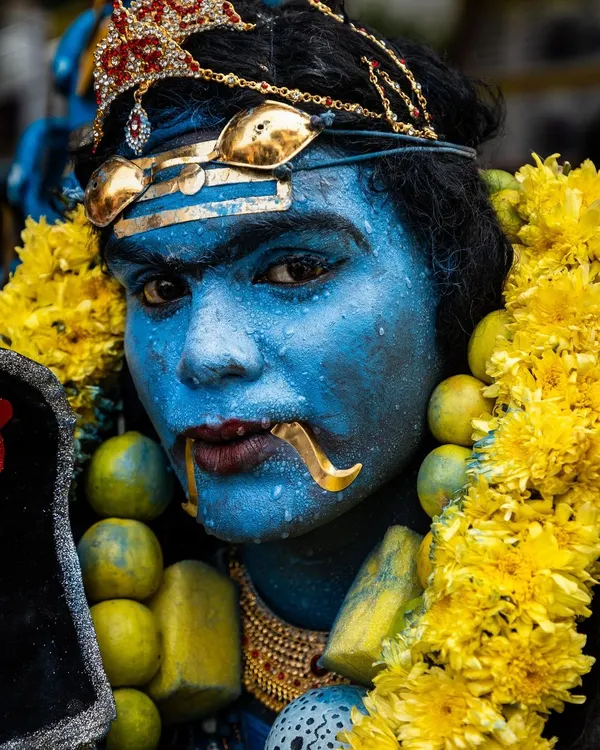 A close-up portrait of a devotee painted blue to represent a deity, his intense gaze and traditional adornments showcasing the festival's transformative power.