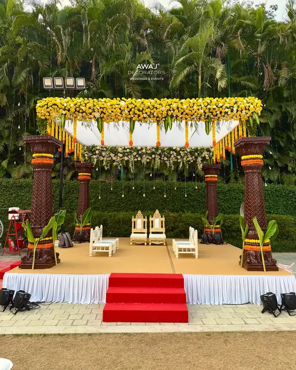 A magnificent traditional mandap for a daytime wedding, featuring ornate pillars, a canopy of yellow marigolds, and elegant seating for the couple and their families.