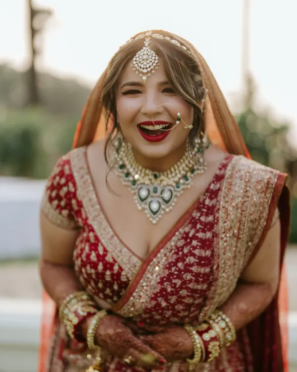 A classic red bridal look complete with a bold red lip and a traditional nath. Her joyful laugh shows she feels as amazing as she looks. This is a timeless choice for any bride.