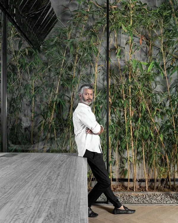 A portrait of me, Ar. Sumit Dhawan, in my element. Here I am leaning against a concrete table with a backdrop of bamboo, reflecting my design philosophy of blending raw, modern materials with natural elements.