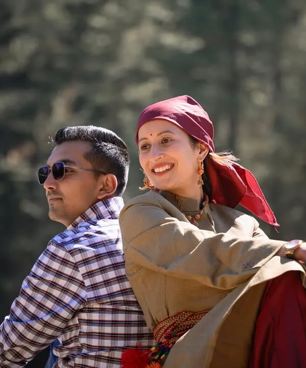 A relaxed portrait of the couple sitting back-to-back, dressed in a mix of traditional and modern attire, symbolizing the beautiful blend of their personalities.