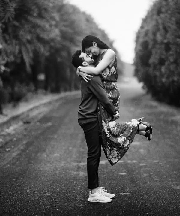 A classic black and white shot of him lifting her up on an empty road. The composition creates a feeling of romance and timelessness, like a scene from an old movie.