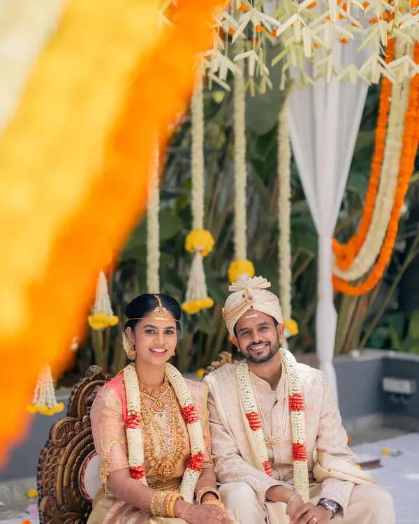 A happy portrait of the bride and groom at their South Indian wedding. The mandap is decorated with traditional flowers, creating a beautiful and authentic setting for their ceremony.