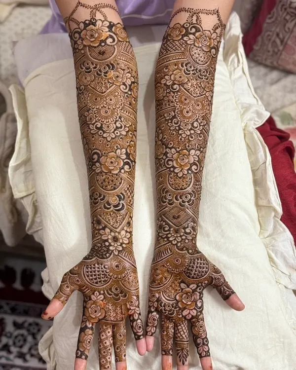 A complete bridal henna design that extends up the full arm. The patterns are a mix of floral motifs, paisleys, and intricate net-work, creating a classic and rich look for the bride.