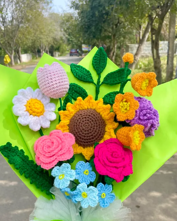 This colorful mixed flower bouquet looks so beautiful in the natural sunlight. It has a sunflower, roses, a tulip, and other pretty blooms, showing how different handmade flowers can come together to create something truly special.