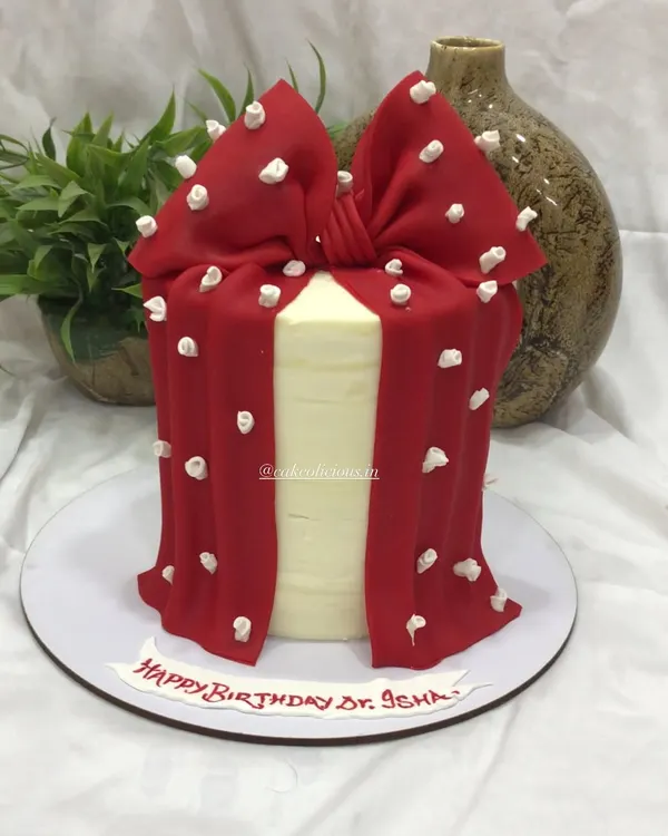 This elegant cake features a dramatic red bow made from fondant, draped over a smooth white ganache base. It's a stylish and modern design that makes a bold statement at any event.