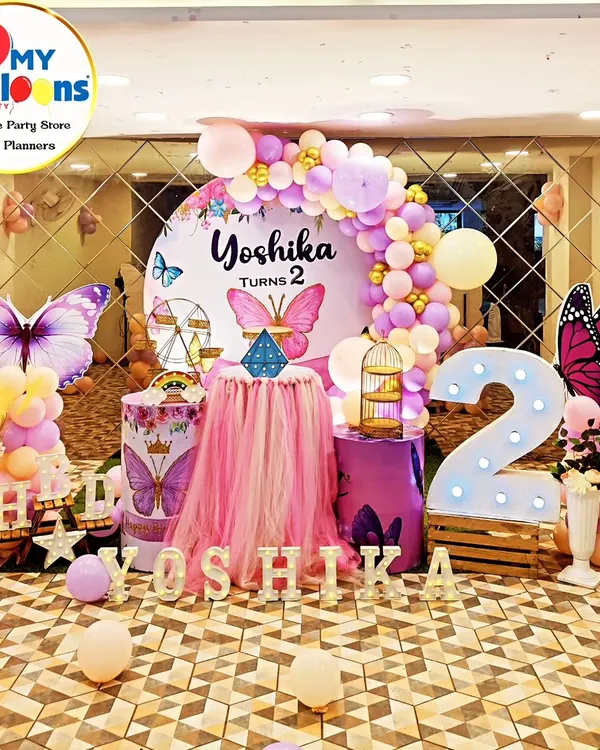 A breathtaking butterfly theme for a second birthday. This setup features a mirrored floor, a central tulle-draped table, large butterfly cutouts, and a pink and purple balloon arch, creating a truly magical atmosphere.