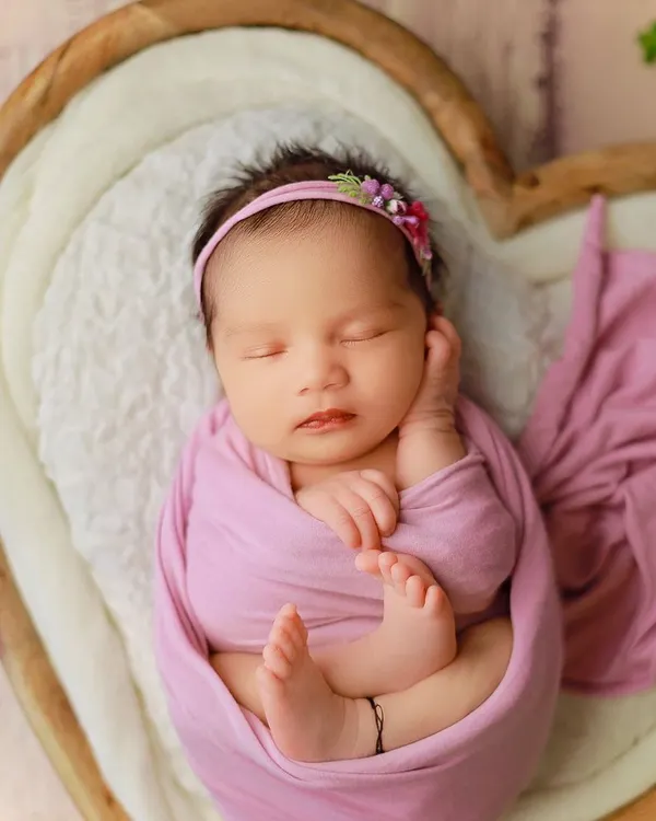 A beautiful 20-day-old baby girl, peacefully asleep. We posed her in a classic womb-like curl within our heart-shaped prop, using a soft purple wrap to add a touch of color.