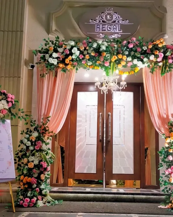 A grand and welcoming entrance for Manasi and Gaurav's wedding at the Regal. The doorway is framed by a lush arch of pastel flowers and soft drapery, with a personalized welcome sign to greet guests.