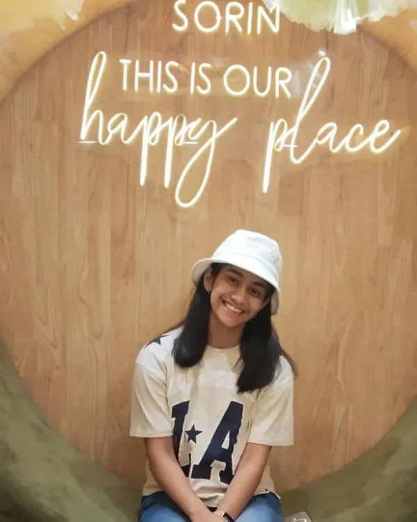 A happy young client posing in our signature photo spot. The "happy place" sign is a favorite for capturing joyful moments.