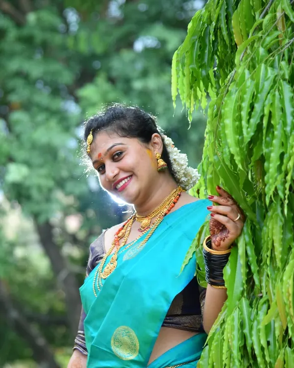 A beautiful outdoor portrait of a woman in a traditional silk saree. Natural light brings out the rich colors of the attire and the warmth of her smile, perfect for any family function album.