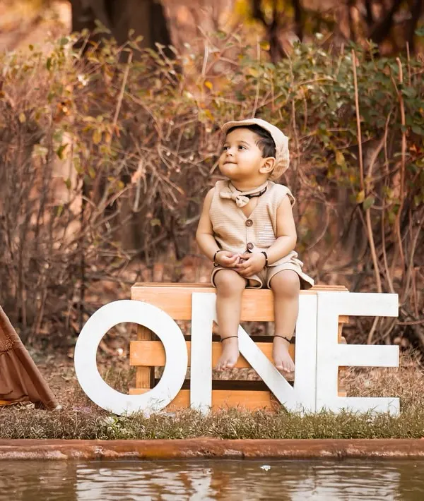 An outdoor first birthday shoot with a rustic, adventurous theme. The 'ONE' sign, teepee, and natural setting create a beautiful backdrop for celebrating this special milestone.