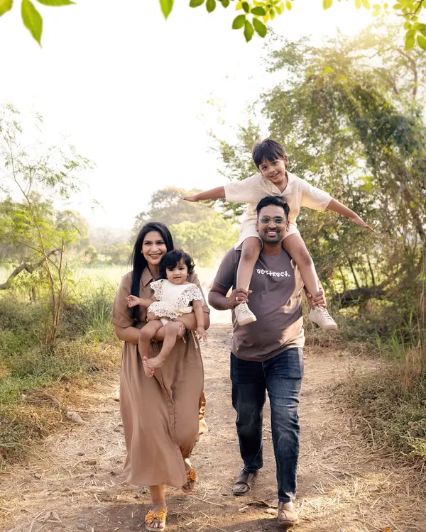 A family takes a walk through a sunlit path, son on his father's shoulders, full of joy. Our outdoor picnic sessions are about capturing your family's adventure.