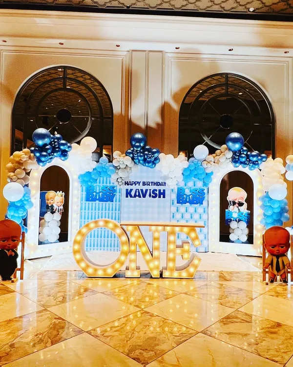 A complete Boss Baby themed stage for a first birthday, featuring character cutouts, city skyline backdrops, and large light-up "ONE" letters.