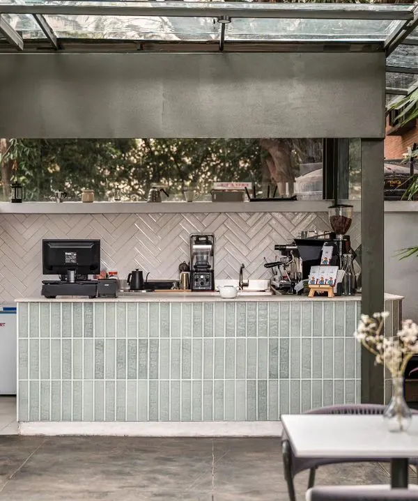 The coffee bar at Kana Cafe, featuring pastel green subway tiles and a white herringbone backsplash. This area is the heart of the cafe, designed with a chic and vibrant appearance to welcome patrons.