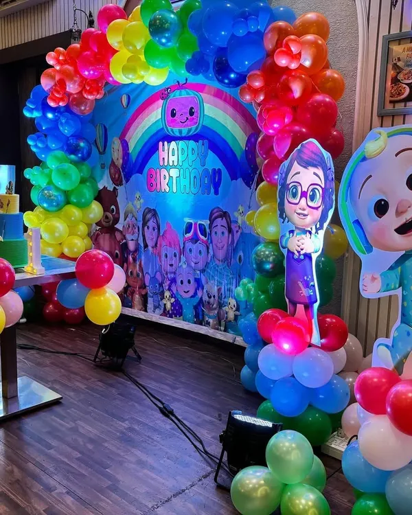 A vibrant Cocomelon theme party setup featuring a rainbow balloon arch over a backdrop filled with all the favorite characters.