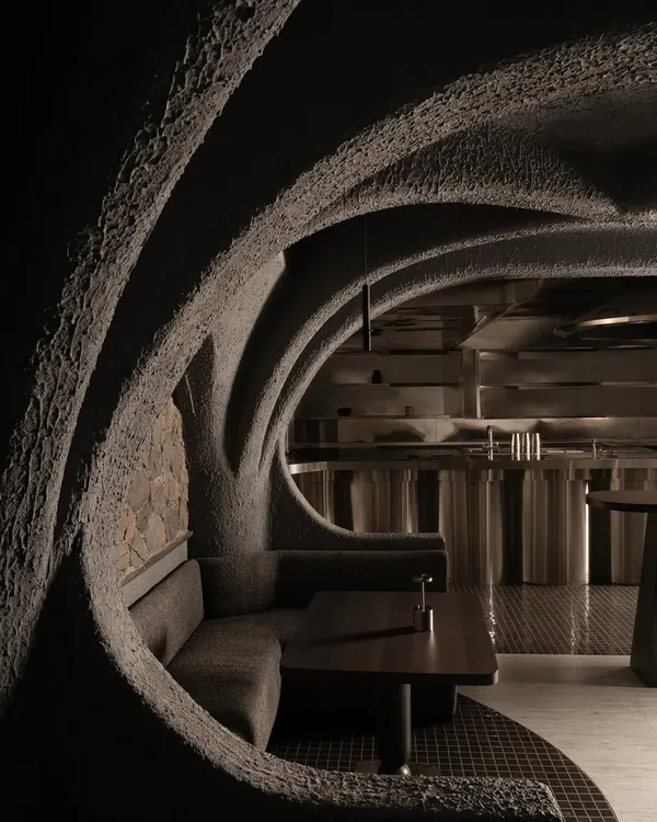 This is a view into the heart of Call Me Ten, a Japanese-inspired restaurant in New Delhi. The design is a study in brutalist poetry, where repeating concrete arches create a rhythmic, cave-like procession, guiding the eye and the body through a narrative of shadow and form.