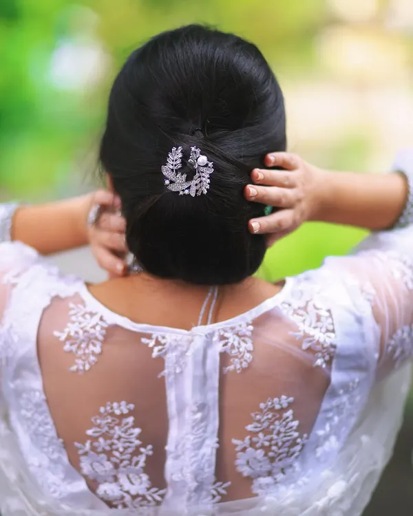 A clean and classic low bun, adorned with a simple yet elegant silver hair accessory. This hairstyle is perfect for a sophisticated guest look with a designer blouse.