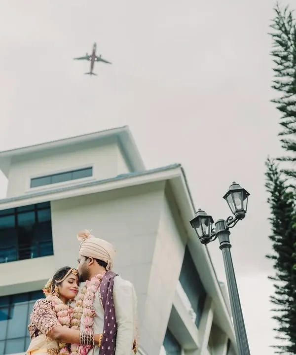 A unique and symbolic shot of the couple in a tender embrace outdoors, as an airplane flies overhead, signifying their journey together.