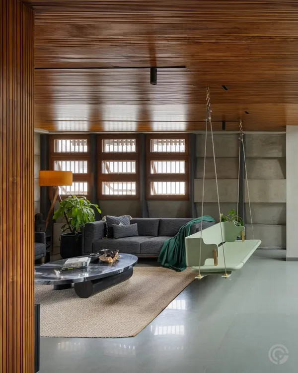 A view of a living space where a modern mint-green swing hangs from a warm wooden ceiling, contrasting with the raw concrete feature wall and smooth grey flooring. This blend of materials and playful elements is central to our design approach for creating dynamic family homes.