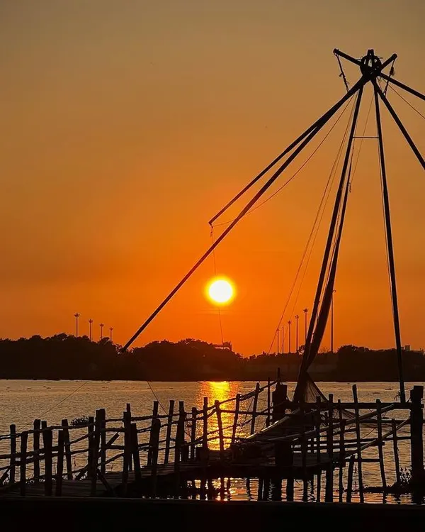 A classic sunset view in Kochi, Kerala, featuring the iconic Chinese fishing net silhouetted against a fiery orange sky. This image captures a unique cultural landscape at the most beautiful time of day.