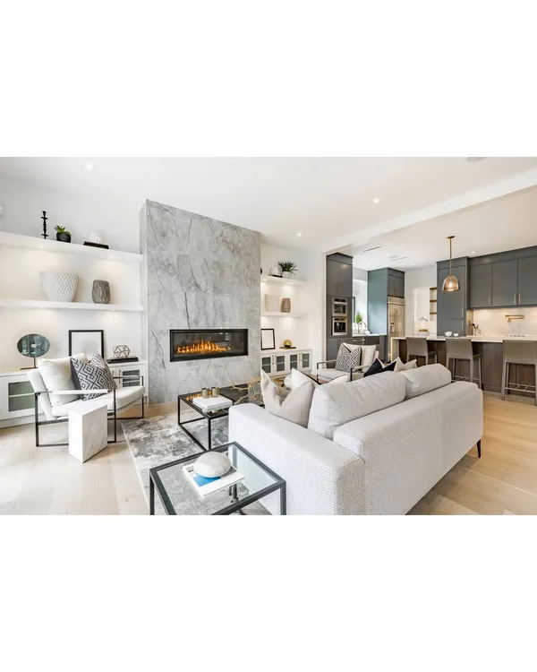 This open-plan living area features a striking marble-clad fireplace as its focal point. The space flows into a modern kitchen, demonstrating how we use materials and layout to connect different functional zones into one harmonious design.