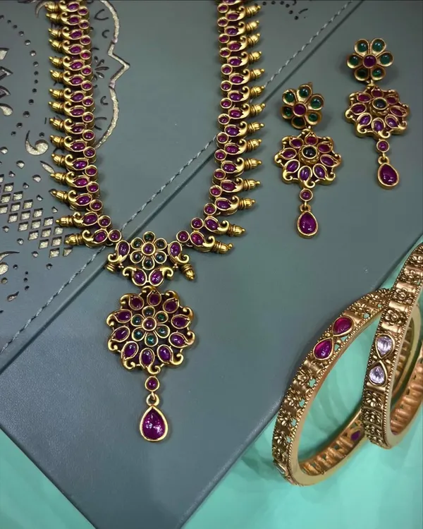 This is a beautiful temple jewellery necklace set with matching earrings and bangles. The rich ruby and green stones give it a classic look, perfect for wearing with silk sarees for a wedding or festival.