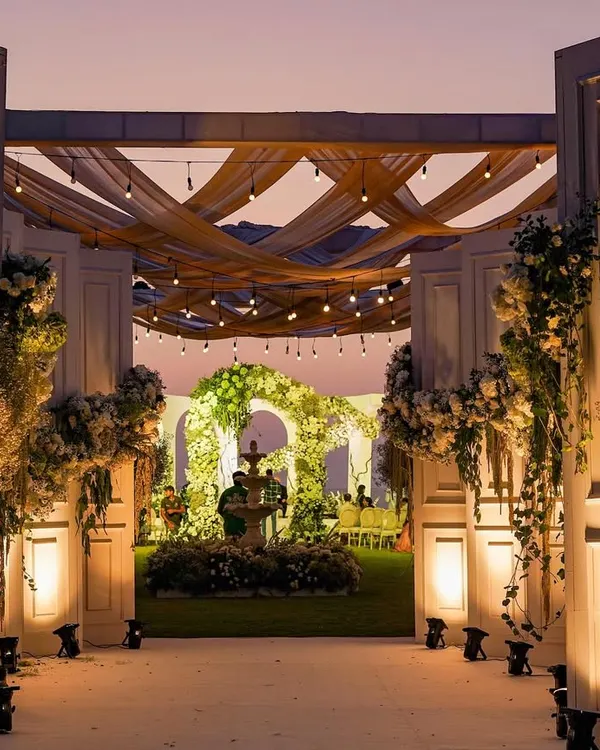 The magical transition from day to night at this white wedding in Goa. The grand entrance, illuminated against the twilight sky, leads to a garden wonderland where the celebration is just beginning.