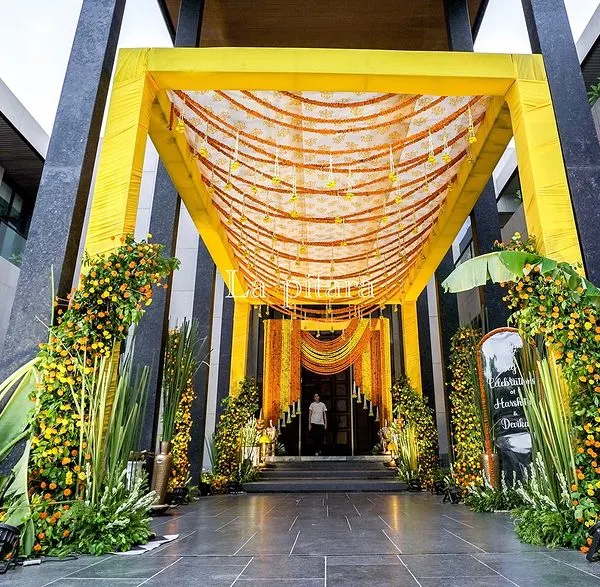 A magnificent entrance for a Teej celebration, featuring a grand yellow canopy adorned with marigold garlands. The entire walkway is lined with lush greenery and floral arrangements, creating an immersive and festive experience.
